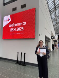 Sanja in front of a large red sign which says 'welcome to BSH 2025' on it